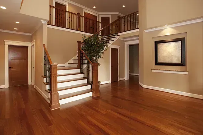 Elegant home interior with hardwood floors, a staircase, and a balcony with a wooden railing, beige walls, and recessed lighting.