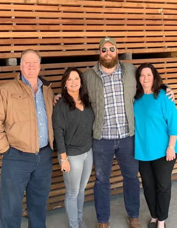 Four people standing in front of a wooden wall, posing for a photo. A man with a beard has his arm around a woman.