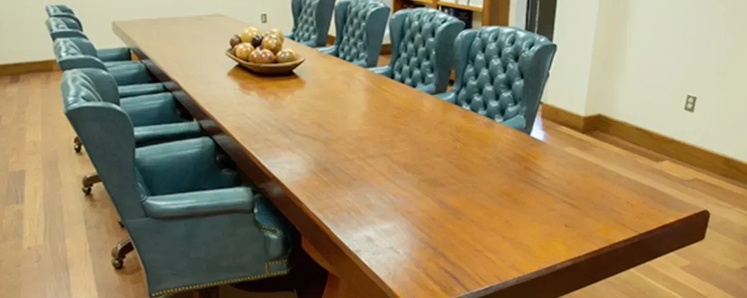 A long, wooden conference table with blue upholstered chairs on each side. A bowl of fruit sits in the middle of the table.