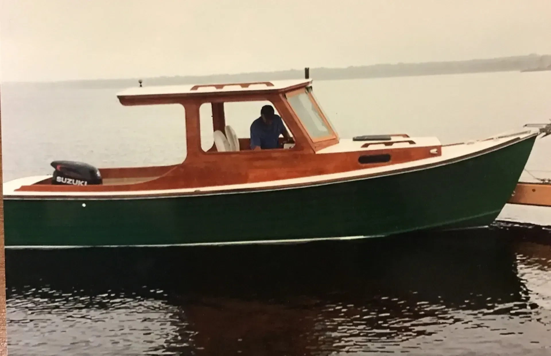 Wooden boat with a green hull and brown cabin on the water; a person is visible inside.
