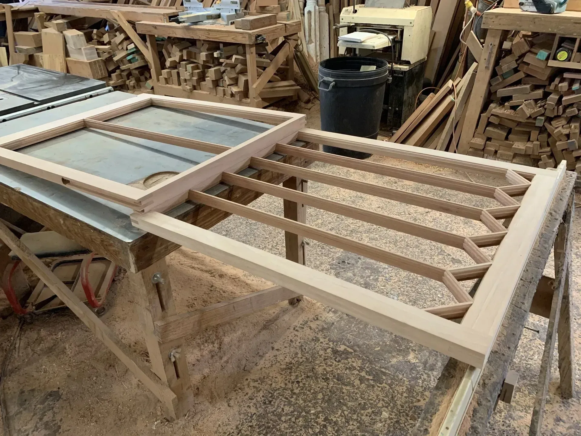 Wooden frame construction on a workshop table, with one frame complete and the other partially assembled.