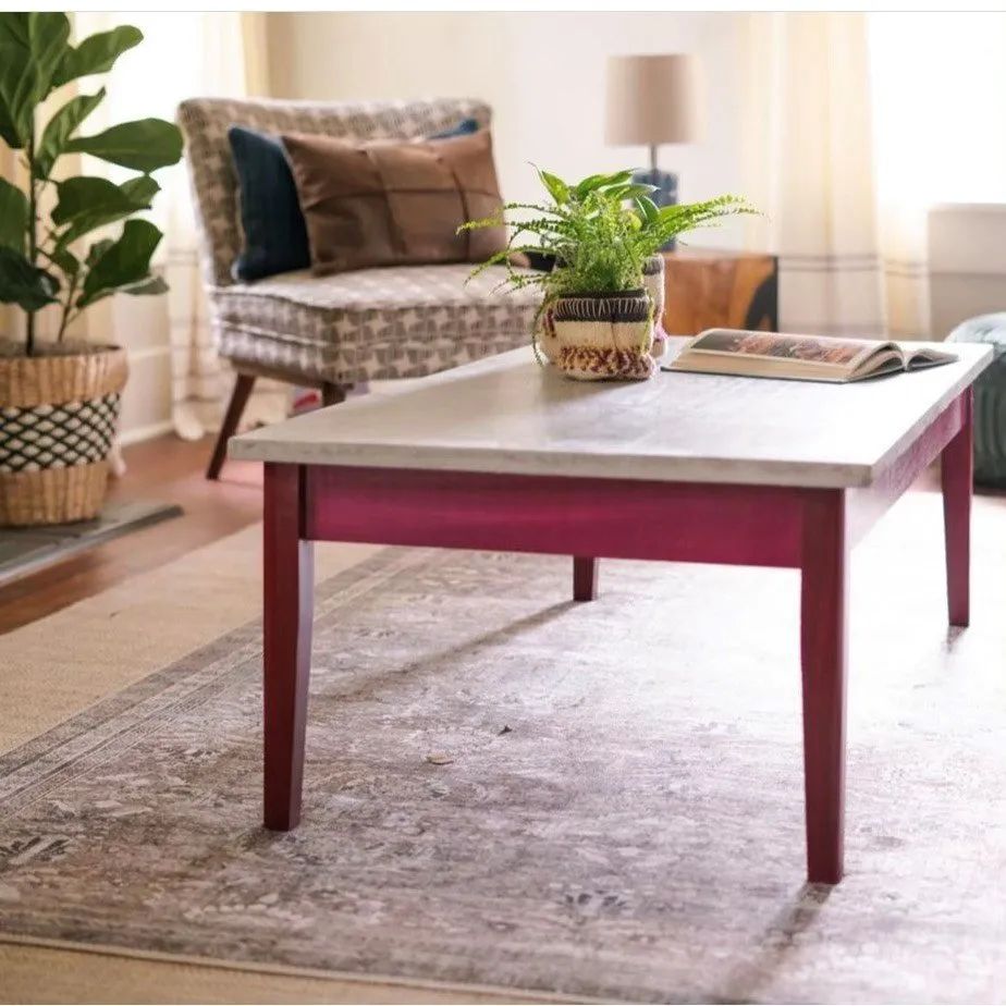 A living room with a magenta-painted coffee table, armchair, and plants on a patterned rug.