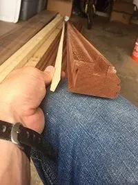 A person holding two pieces of wood. One is a thin, light-colored piece, the other is a thick, reddish-brown frame.