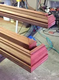 Close-up of two wood pieces with angled corners, showing the end grain of pinkish-red wood. The pieces have a brown grooved and layered design.