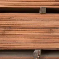 Stack of reddish-brown wooden planks, likely lumber, neatly organized.