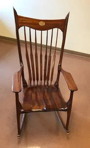 Dark wood rocking chair with a high back and curved arms, indoors on a brown floor.