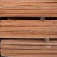 Stack of reddish-brown wooden planks, likely lumber, piled on a pallet, ready for use in construction.