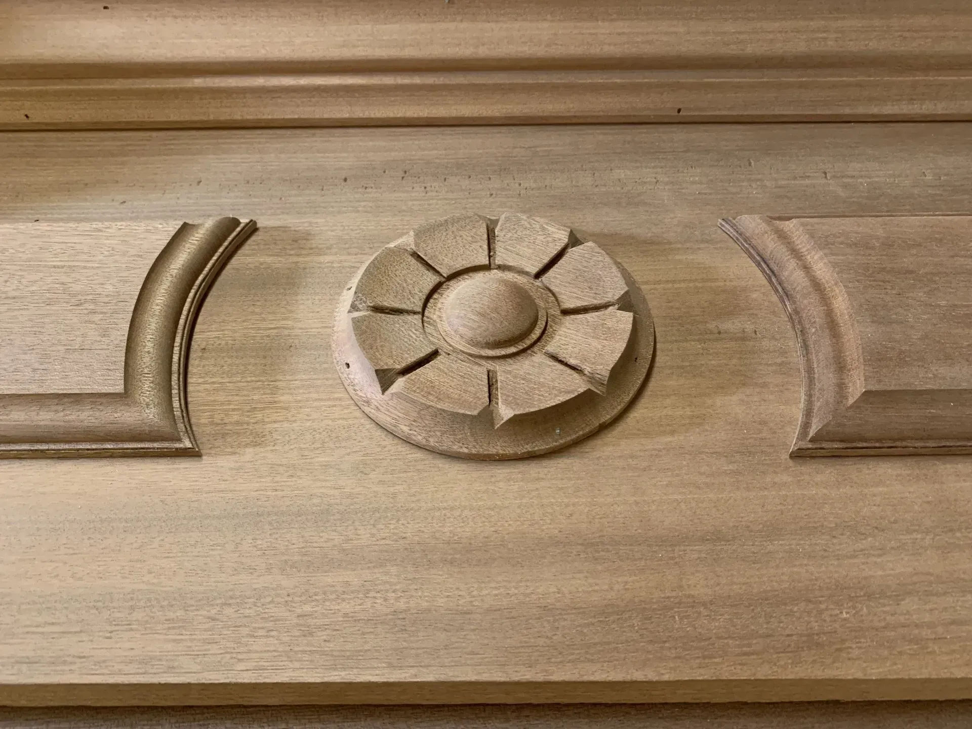 Wooden panel with carved floral rosette centered between architectural elements, showing a distressed, neutral finish.
