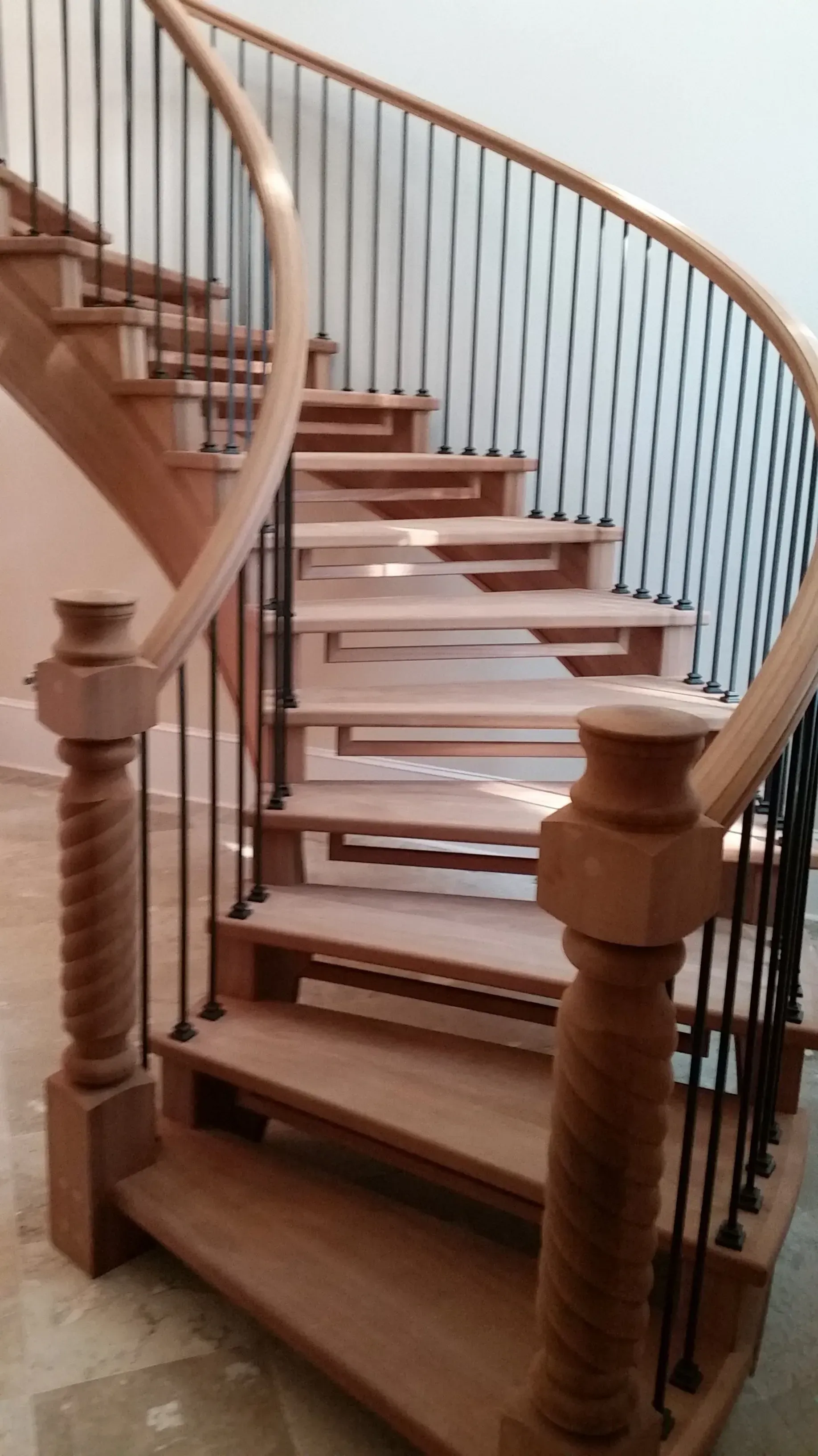 Wooden curved staircase with black metal balusters and detailed wooden posts. The stairs are in a home.