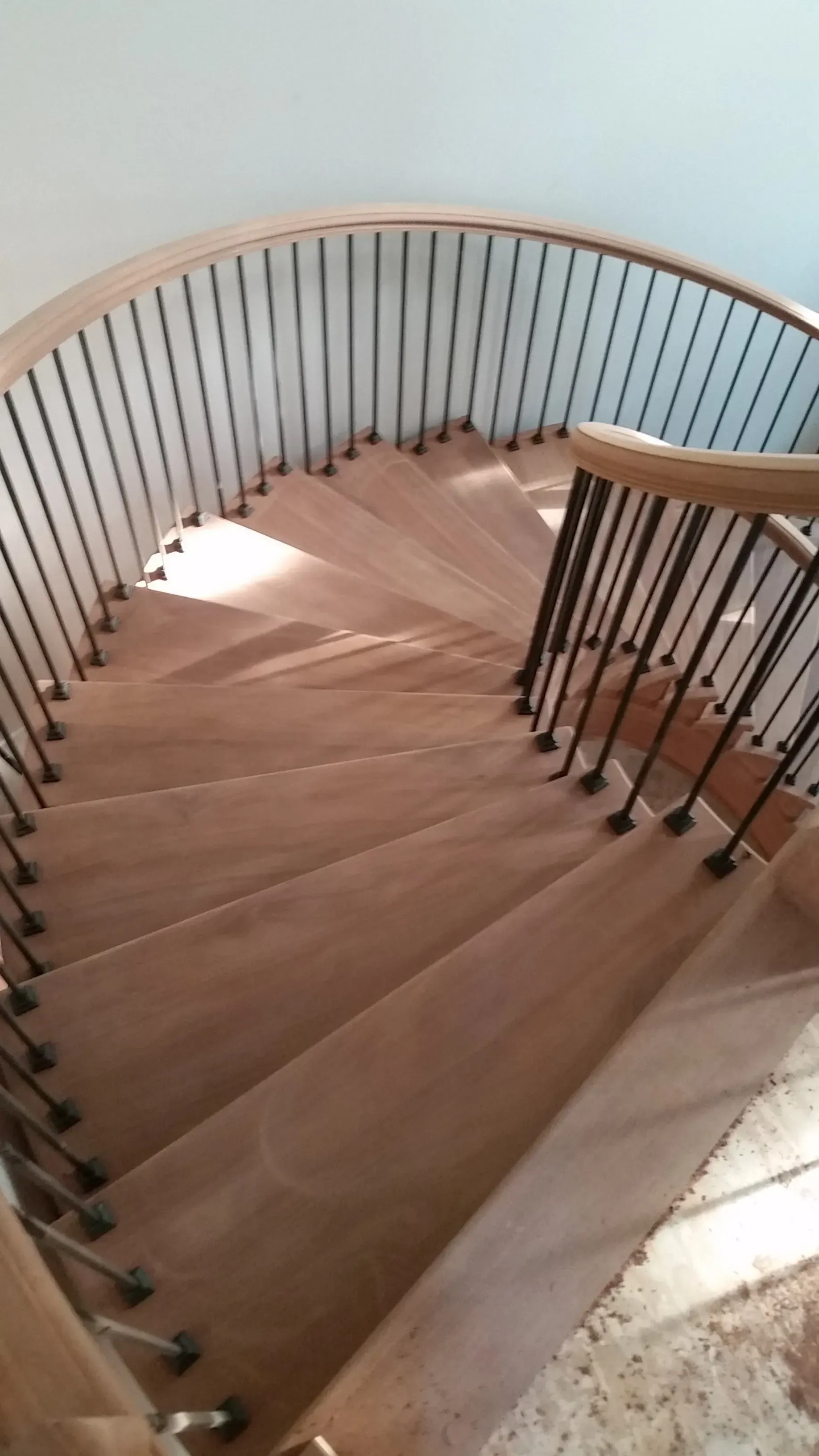 Wooden spiral staircase with black metal railings.  Light streams down, highlighting the wood grain on the steps.