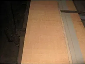 Wooden planks, possibly flooring, in a dimly lit interior setting. Light brown wood with a visible seam.