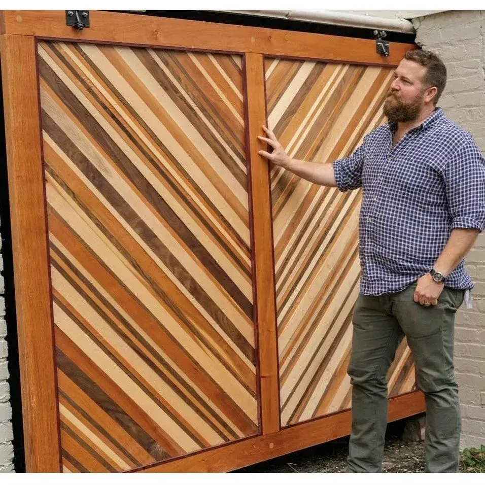 Man standing next to a large wooden sliding door with diagonal planks in various wood tones. The door is mounted on a track.