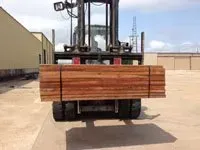 Forklift carrying a bundle of wooden planks, outdoors on a concrete surface.