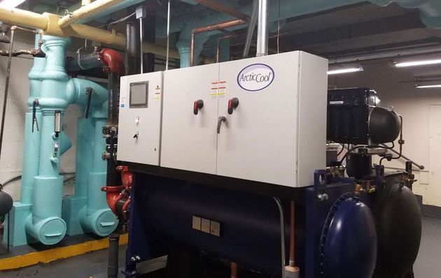 Industrial mechanical room with a large, white electrical control panel mounted on a dark blue chiller unit.