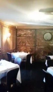 A dining room with white-clothed tables, dark chairs, and wood-paneled walls featuring historical-style artwork.