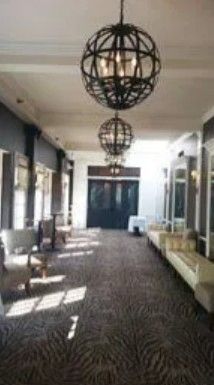 A long hotel hallway with patterned carpets, two large spherical chandeliers hanging from the ceiling, and side seating.