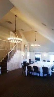 A dining room with a long table, chairs, two large circular chandeliers, and a staircase with a wooden railing.