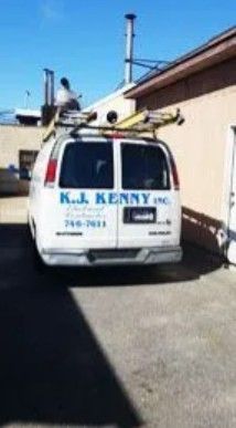 A white K.J. Kenny Inc. work van parked in a lot, with ladders secured on a roof rack.