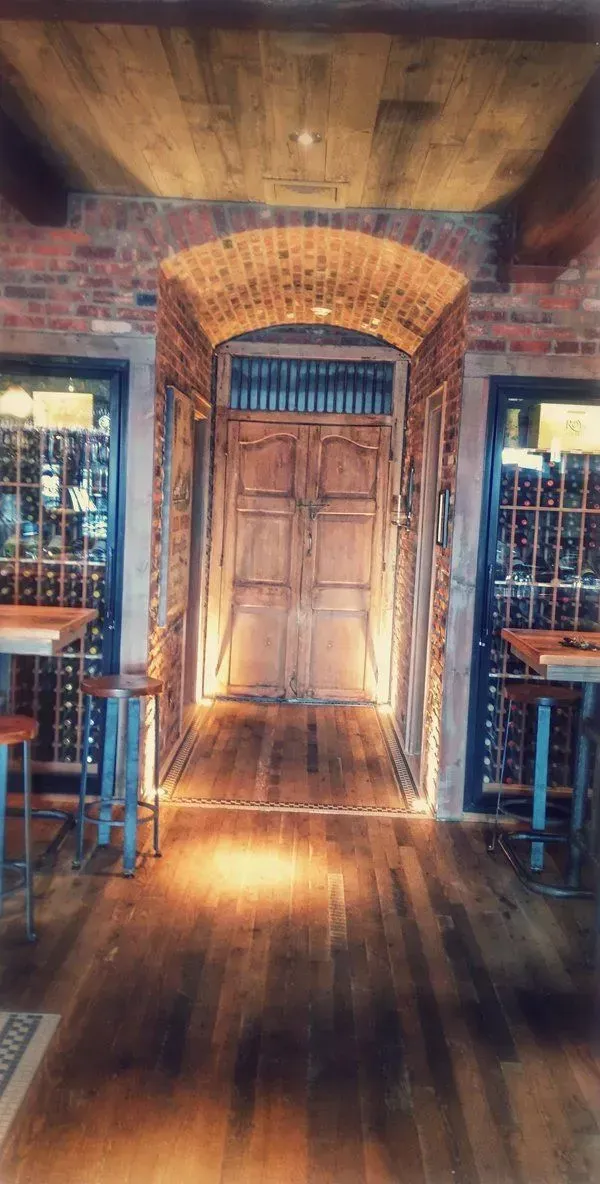 A rustic wine cellar features a central wooden double door framed by an arched brick ceiling, flanked by glass wine cases.