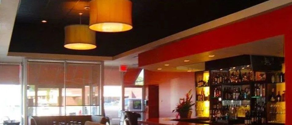 A modern restaurant bar with two hanging drum lights, a black ceiling, and a bright red wall accent.