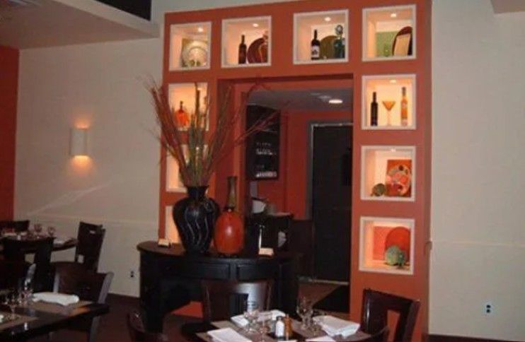 A restaurant interior featuring a central terracotta-colored wall with recessed, illuminated display niches.
