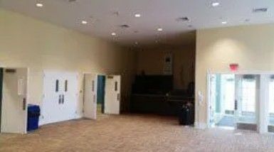 A large, empty room with beige walls, a patterned carpet, recessed ceiling lights, and multiple white double doors.