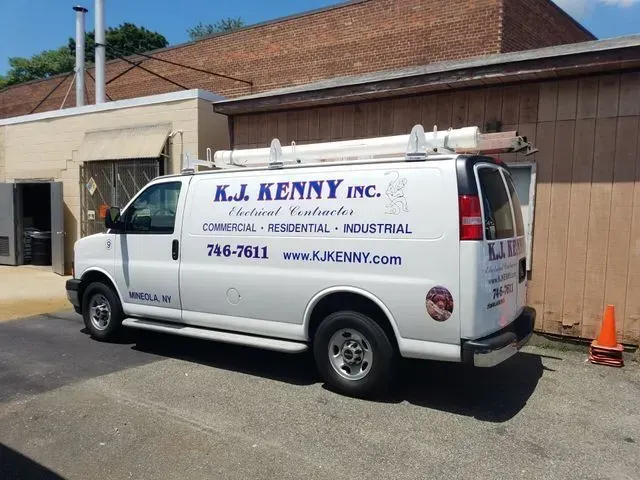 A white K.J. Kenny Inc. electrical contractor van parked in front of a brick building.