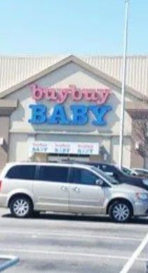 A silver minivan parked in front of a storefront with a large 