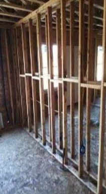 Interior view of a residential construction site featuring newly framed wooden stud walls and a plywood floor.