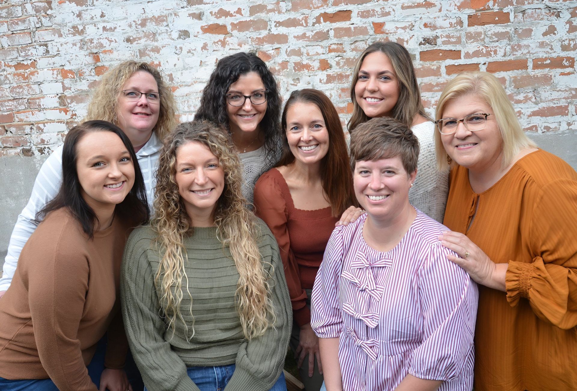 Group of eight people posing in front of a brick wall, smiling.