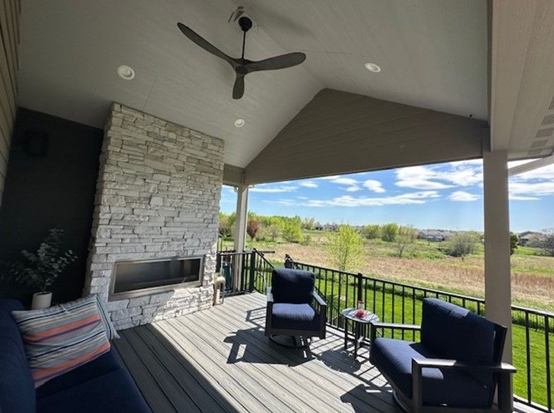 A porch with a fireplace, chairs, and a ceiling fan.