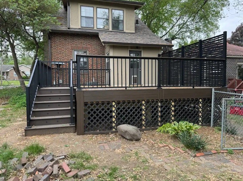 Backyard deck with dark brown steps, railing, and lattice. Wooden siding and brick wall.