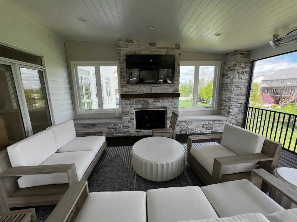 Outdoor living room with white sofas, fireplace, TV, and views.