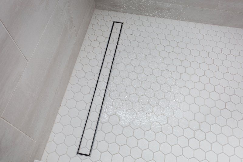 A shower stall with white tiles and a black drain.