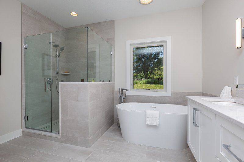 A bathroom with a tub , sink , shower and window.