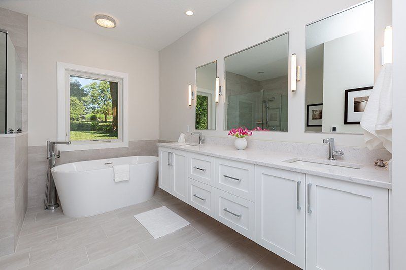 A bathroom with a tub , sinks , mirrors and a window.