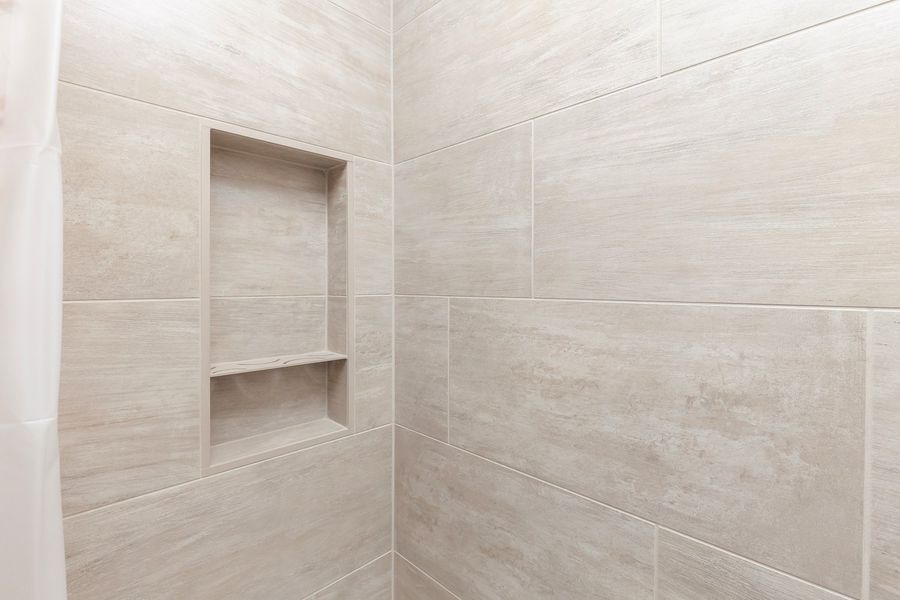 A shower with a shelf in the wall and a shower curtain.