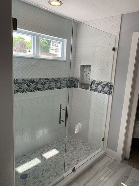 A bathroom with a walk in shower with a glass door and a window.