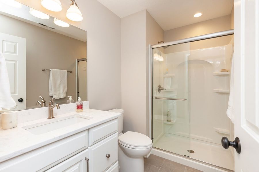 A bathroom with a toilet , sink , mirror and shower.