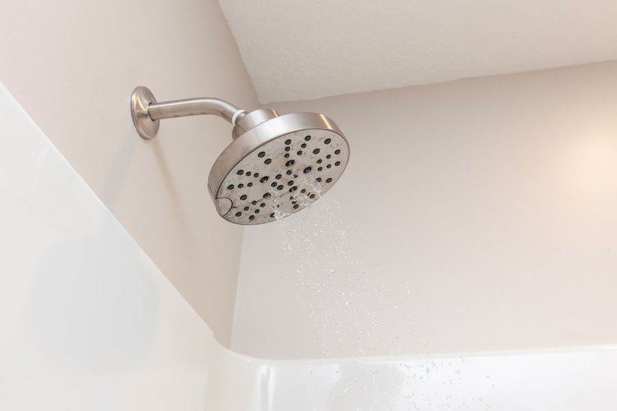 A shower head is hanging from the ceiling in a bathroom next to a bathtub.