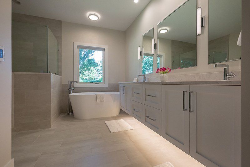 A bathroom with a tub , sinks , mirrors and a window.
