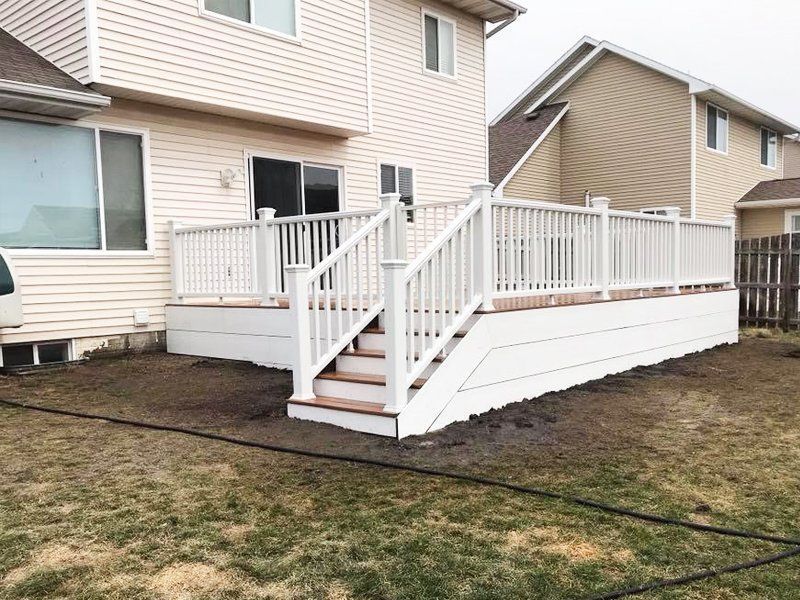 A white deck with stairs is in the backyard of a house.