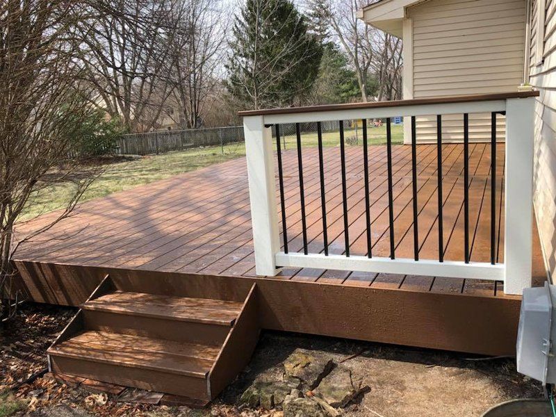 A wooden deck with stairs and a white railing in front of a house.