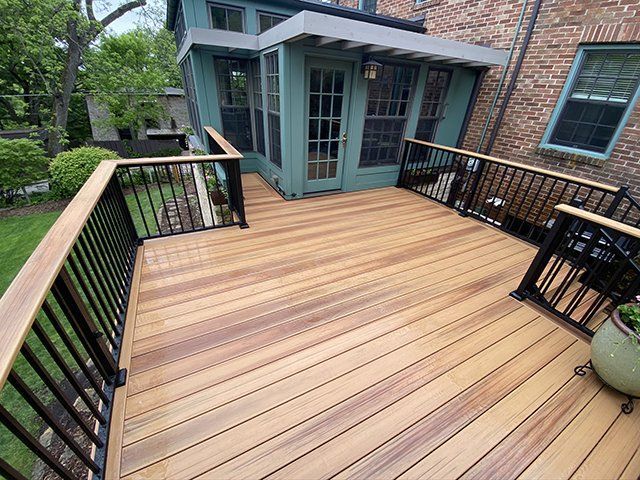 A wooden deck with a black railing and a brick house in the background.