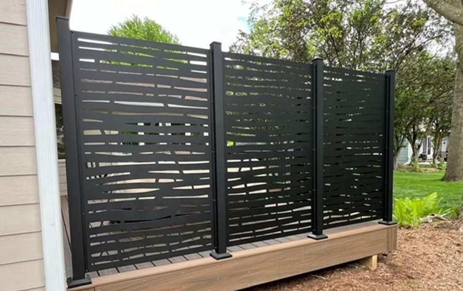 A black fence is sitting on a wooden deck next to a house.
