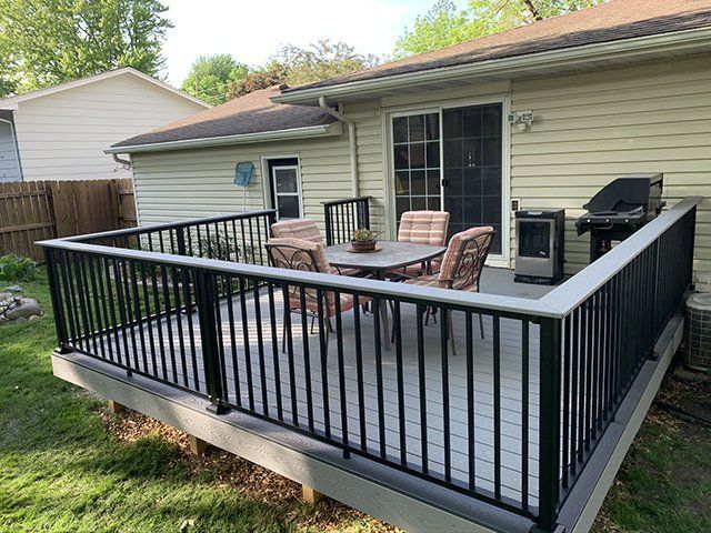 A deck with a table and chairs on it in front of a house.