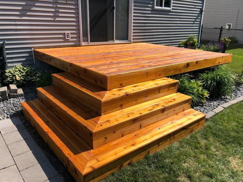 A wooden deck with stairs leading up to it in front of a house.