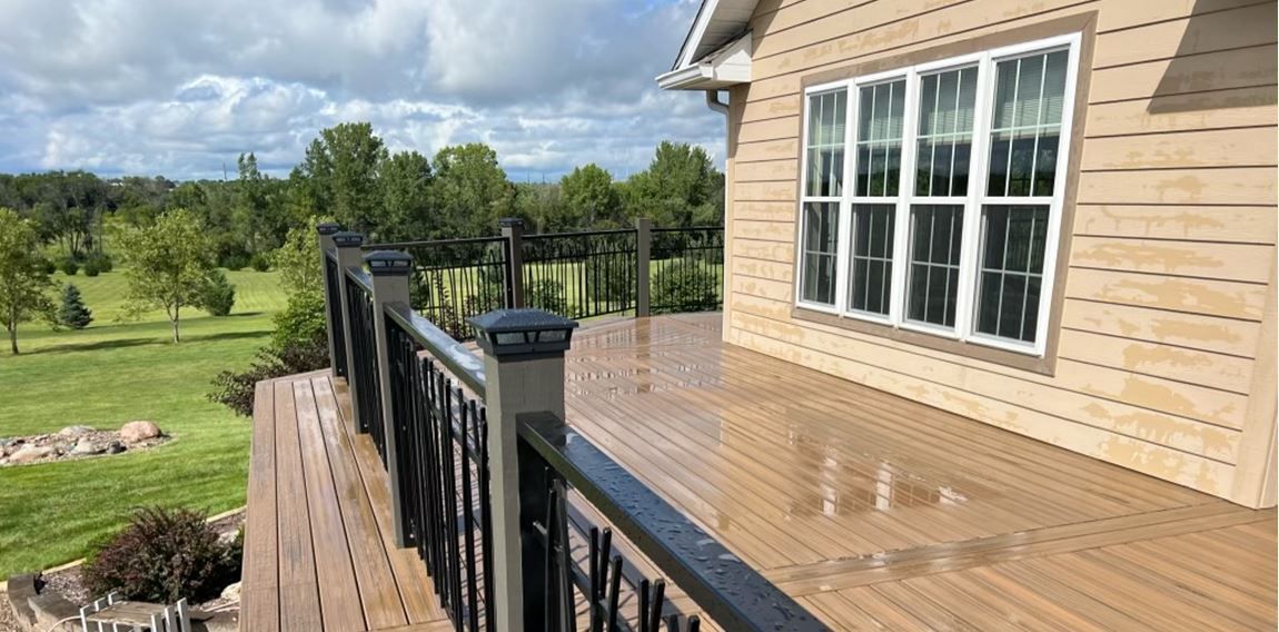 A large deck with a railing and a window on the side of a house.