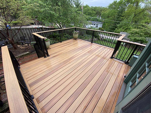 A wooden deck with a black railing and trees in the background.