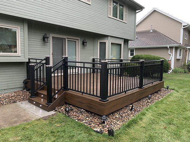 A large deck with a black railing is in the backyard of a house.